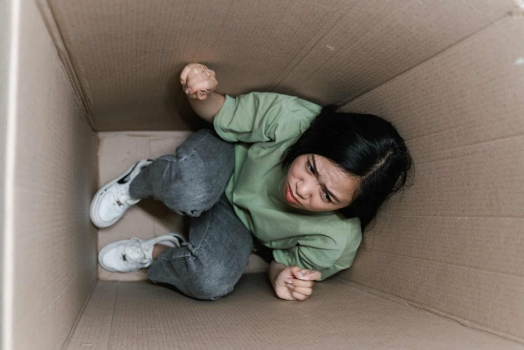 A fearful woman having claustrophobia in a cardboard box